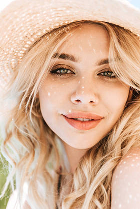 美丽的年轻金发女人的肖像在草帽微笑着在相机