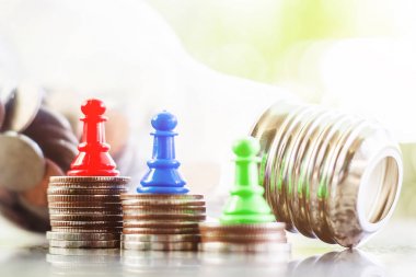 棋典当在硬币的顶部和电灯泡瓶形状反对模糊的自然绿色背景为投资、商业、财政和省钱概念 棋典当在硬币的顶部和电灯泡瓶形状反对模糊的自然绿色背景为投资、商业、财政和省钱概念