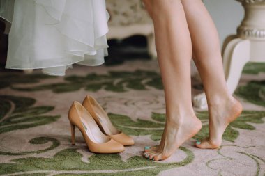 美丽的新娘的腿旁边的高跟鞋和白色婚纱礼服