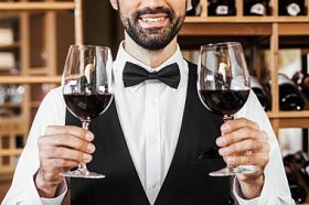 在葡萄酒店里拿着两杯红酒的微笑年轻的侍酒师拍的照片
