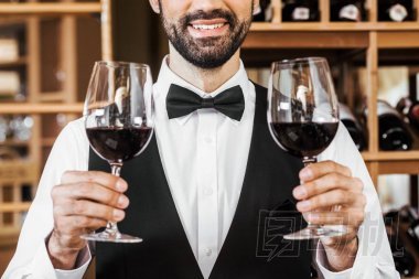 在葡萄酒店里拿著兩杯紅酒的微笑年輕的侍酒師拍的照片