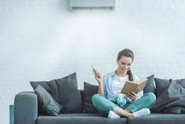 在家中使用遙控器打開空調(diào)的快樂女人看書