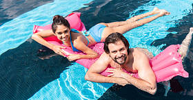 年轻的微笑夫妇游泳在粉红色充气床垫池