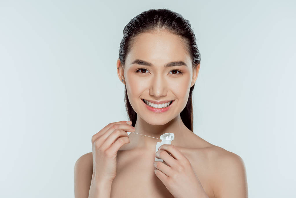 迷人的微笑亚洲女孩手持牙线, 孤立的灰色
