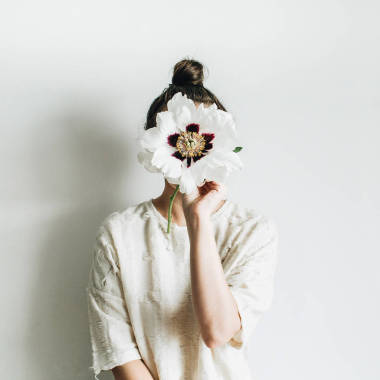 年輕漂亮的女人在白色的背景上舉行白色牡丹花。最小的美容理念