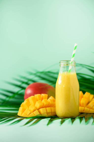 美味的果汁与橙果和芒果在绿松石背景。复制空间。流行艺术设计, 创意夏日概念。绿棕榈叶玻璃瓶中的鲜