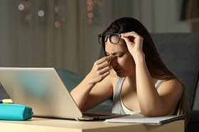 疲惫的学生在网上学习与笔记本电脑在晚上在家中遭受眼睛疲劳