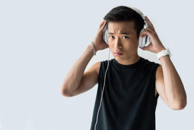 嚴(yán)肅的亞洲運(yùn)動(dòng)員戴上耳機(jī)在灰色背景下被隔離