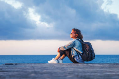 一個美麗快樂的年輕女子的肖像坐在一個木碼頭上的海洋背景和美麗的日落和欣賞的風景