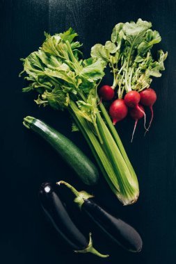 灰黑餐桌上芹菜、蘿卜、茄子的頂部