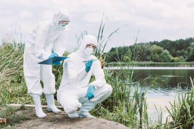 兩名科學(xué)家在保護(hù)面具和西裝檢查在河邊剪貼板上的魚和書寫 