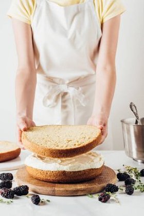 裁剪拍摄的女人做美味的分层蛋糕白色