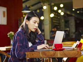 年轻的亚洲妇女坐在咖啡店工作使用笔记本电脑