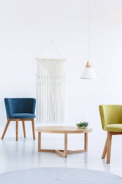 桌在蓝色和黄色扶手椅之间在白色客厅内部与灯。真实照片