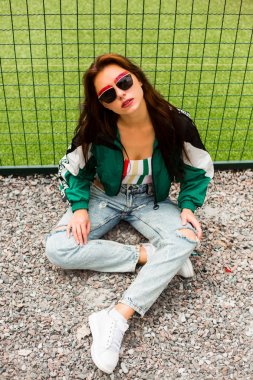 女孩服装的肖像90s 体育风格, 夹克, 牛仔裤香蕉, 太阳镜, 运动场住宅区 女孩服装的肖像90s 体育风格, 夹克, 牛仔裤香蕉, 太阳镜, 运动场住宅区