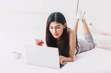 婦女網(wǎng)上購物與筆記本和信用卡在床上在家