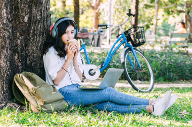婦女放松和喝咖啡與膝上型計算機(jī)坐在草在公園