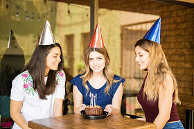 戴着派对帽的漂亮年轻女子在餐厅和朋友一起庆祝生日