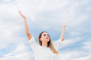 美丽的年轻女子沉思与举手在多云的天空前