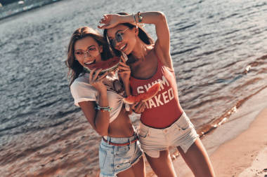在海灘附近河邊水站立的年輕婦女微笑和吃西瓜