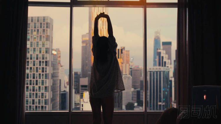 年輕修長的女人的剪影站在大窗口, 伸出手, 早上醒來在日出