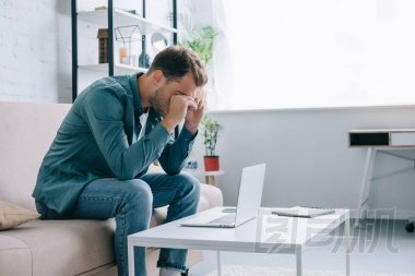 在家使用筆記本電腦的年輕人擦眼睛