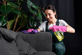 微笑的年轻妇女在橡胶手套清洁沙发用抹布和洗涤剂喷雾