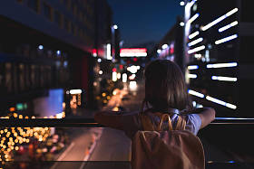 后面的妇女与背包站在街上, 看夜城灯