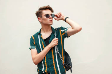 英俊的年輕人在一個時髦的沙灘襯衫調(diào)整太陽鏡在海灘附近綠色墻