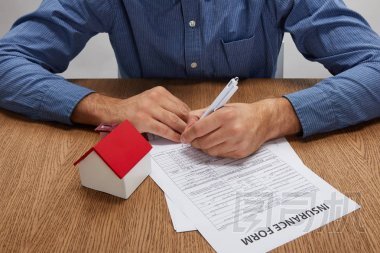 木桌上的人簽保險(xiǎn)表與房屋模型的裁剪