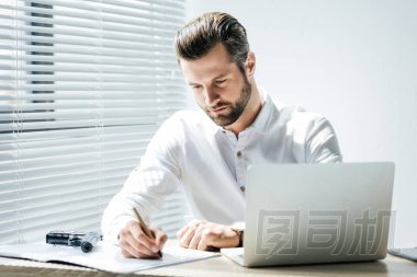 集中的商人寫在文件, 而坐在工作場(chǎng)所用手提電腦和槍