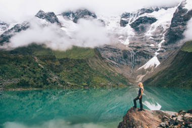 年轻女子游客站在山上的岩石上欣赏高山的自然环境, 在旅途中覆盖着白云。女性旅行者主动穿衣探索美的 Salkantay