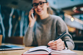 选择关注女手, 在大学图书馆学习的成功女学生在教科书中写论文, 并在教科书中与朋友沟通, 并通过现代智能手机应用与朋友沟