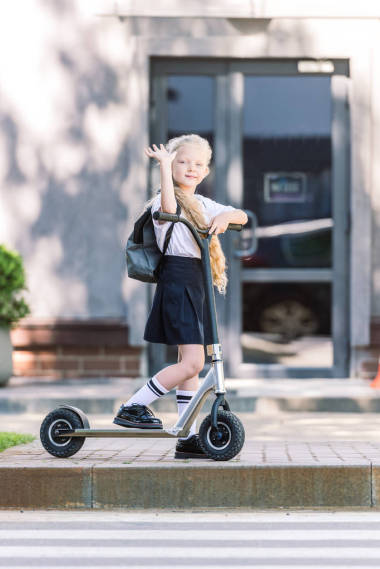 可爱的已经做与背包骑摩托车, 挥舞着手, 看着在街上的相机