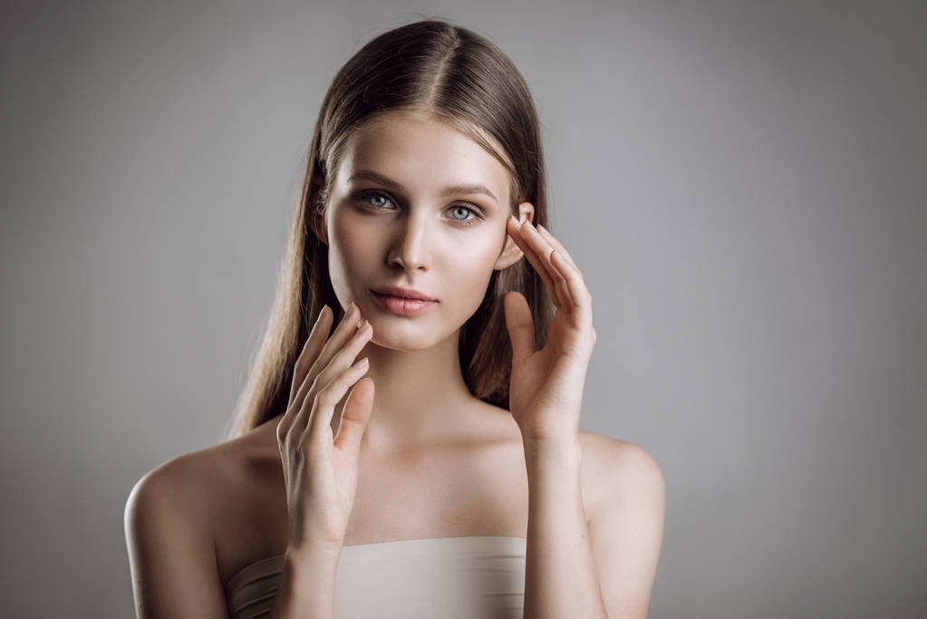 一个美丽的年轻女孩的肖像与裸体化妆在工作室灰色背景