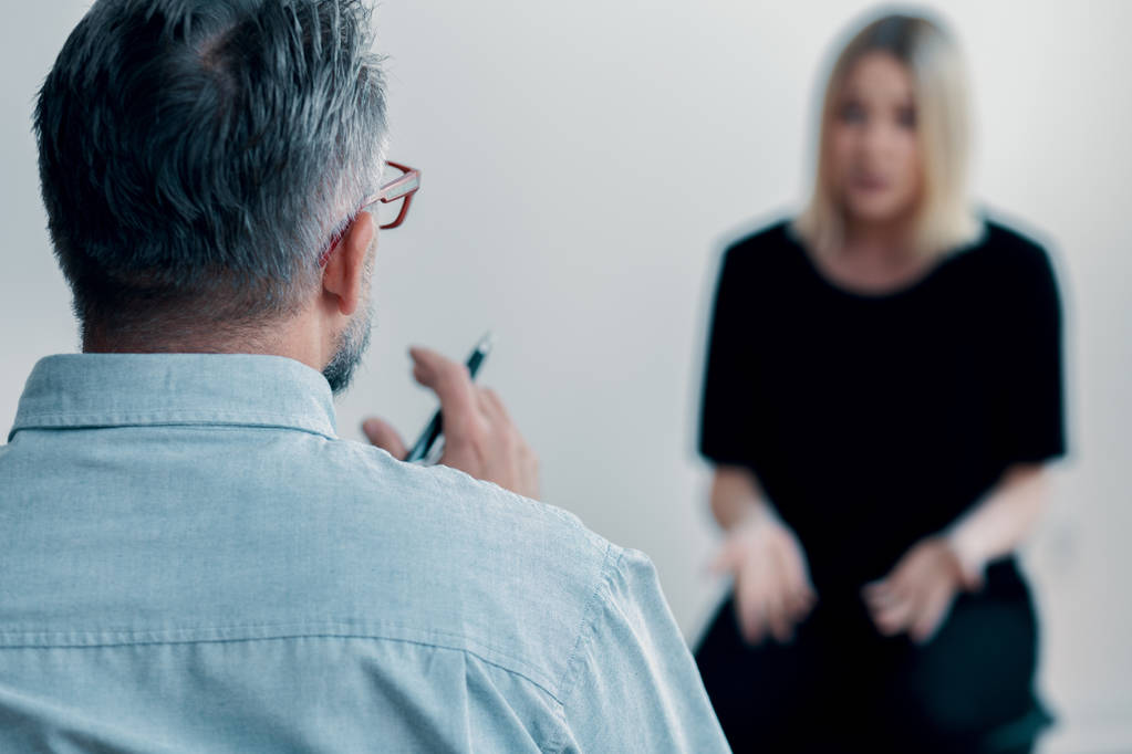 一个治疗师拿着笔和他模糊的女性病人谈话的特写
