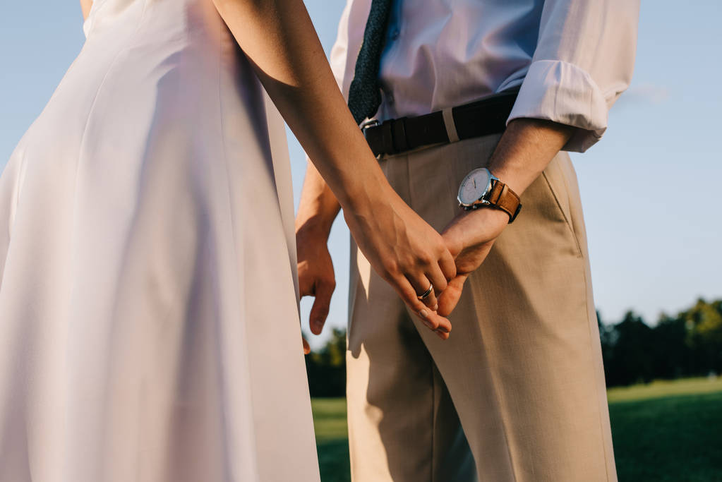 在公园里牵手的浪漫年轻夫妇的裁剪镜头