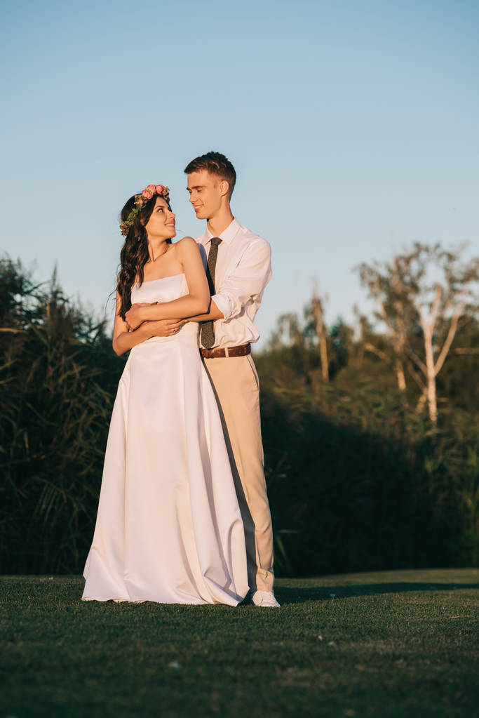 美丽快乐的年轻新婚夫妇拥抱和微笑在公园里彼此  美丽快乐的年轻新婚夫妇拥抱和微笑在公园里彼此
