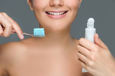 用牙刷和牙膏管在灰上分离的微笑妇女的部分看法 用牙刷和牙膏管在灰上分离的微笑妇女的部分看法