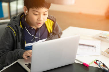 亞洲逗人喜愛的男孩使用筆記本電腦與陽光在早晨在家