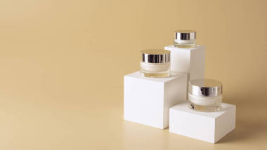 在米色背景上對白色立方體上的玻璃罐子上的面部和身體霜的特寫視圖