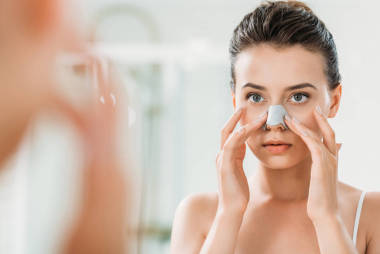 迷人的女孩應(yīng)用鼻子帶和看鏡子在洗手間  