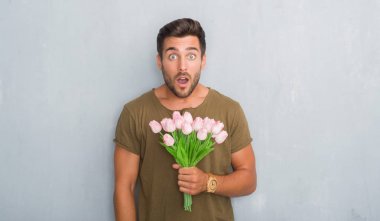 英俊的年轻人在灰色的垃圾墙壁举行花花束惊吓以惊奇面孔, 害怕和激动以恐惧表达