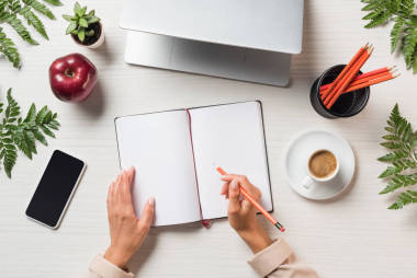 筆記本電腦、智能手機和蕨類樹葉桌上空課本中女性自由職業(yè)者寫作的裁剪圖像