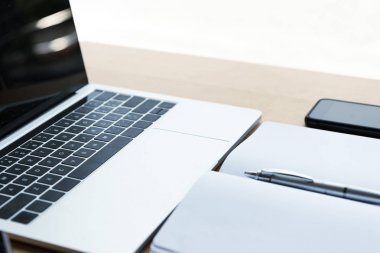 桌面上有鋼筆、智能手機和筆記本電腦的空白筆記本的特寫視圖