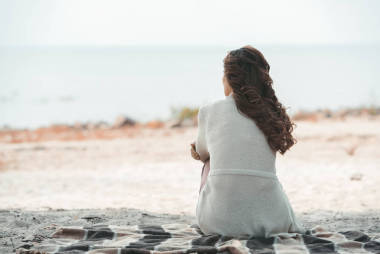 在沙滩上独自躺在毯子上的女人的后视图