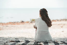 在沙滩上独自躺在毯子上的女人的后视图