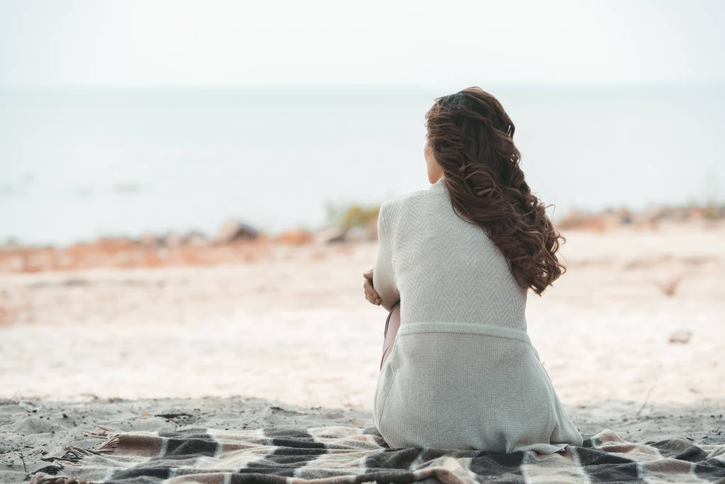 在沙滩上独自躺在毯子上的女人的后视图