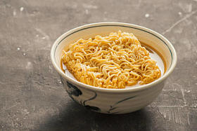 方便面在碗和蔬菜边菜在石头背景。快餐食品概念