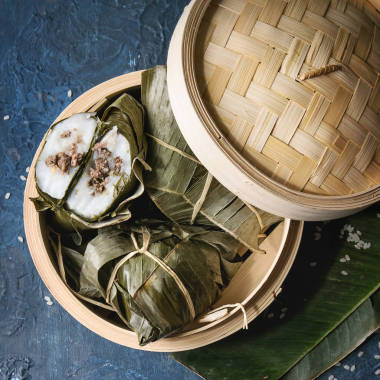 亞洲大米 piramidal 從大米木薯粉中蒸餃子, 香蕉葉中的肉餡在竹蒸籠上, 上面有藍(lán)色的紋理背景。頂部視圖, 空間。方形圖像